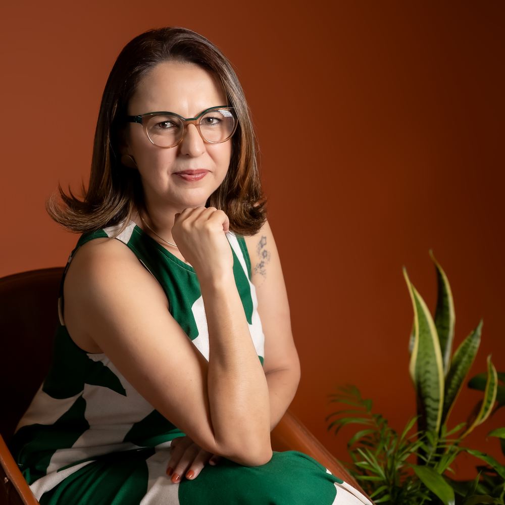 Grazy, da Ideias Verdes, sentada em poltrona com plantas ao fundo